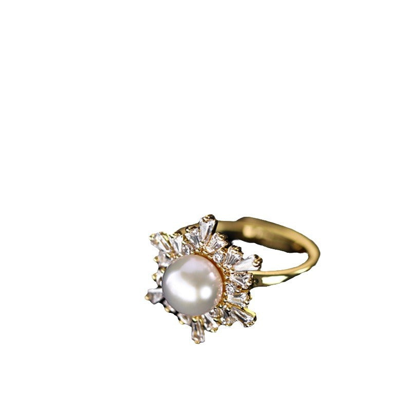 A gold ring featuring a central white pearl surrounded by small clear baguette and round stones, shown on a plain white background.