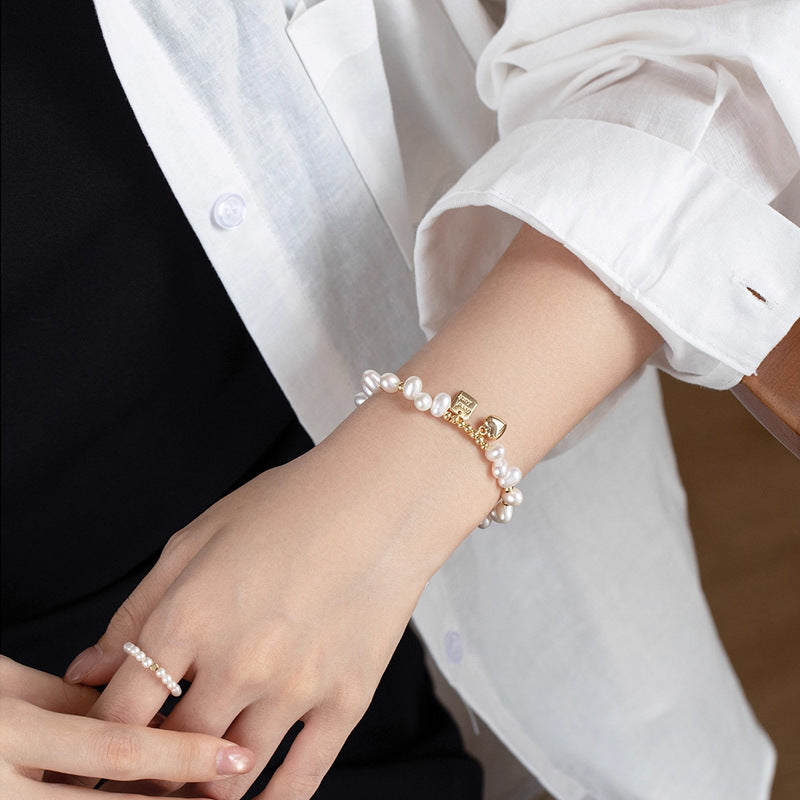 Person wearing a pearl bracelet and ring with a white shirt and black background