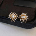 A pair of gold starburst stud earrings with white faux pearls and clear rhinestones, displayed on a black velvet jewelry box.