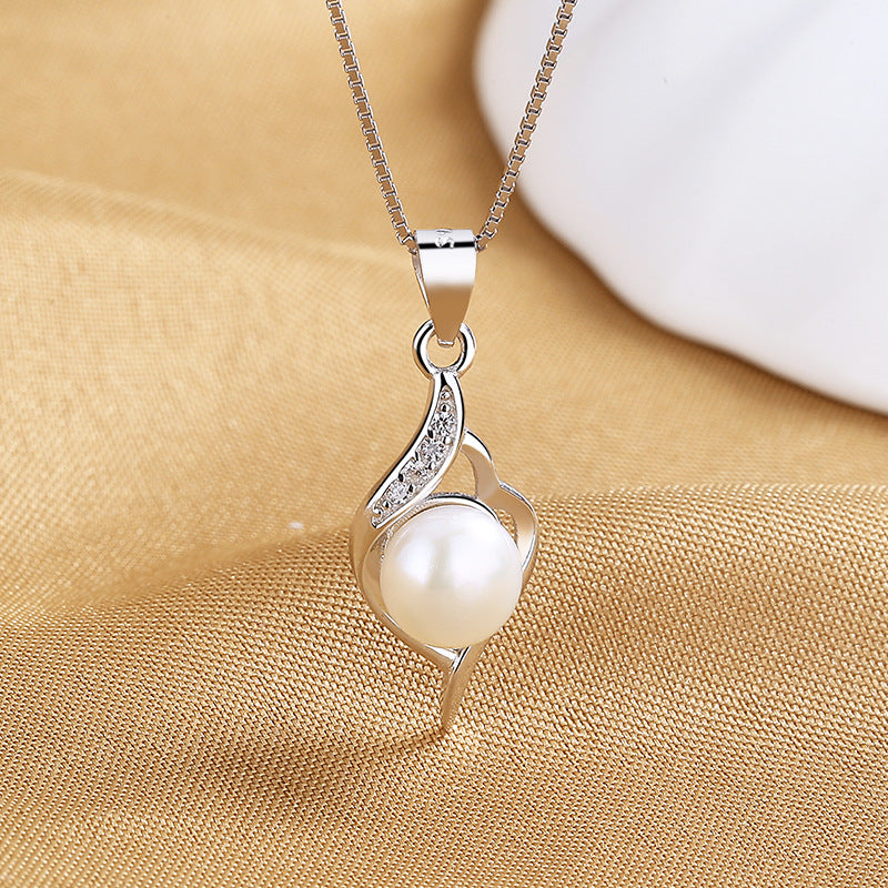A silver pendant necklace featuring a round white pearl and small clear stones, displayed on a textured gold fabric background.