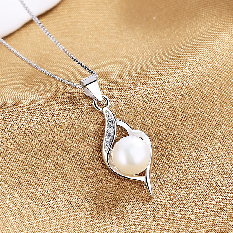 A silver pendant necklace featuring a white pearl set within a leaf-shaped design, displayed on a textured gold fabric background.